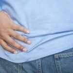 A person in a blue shirt and jeans clutching their hip, possibly indicating pain.