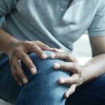 Close-up of a man holding his knee, capturing a moment of discomfort in a casual indoor setting.