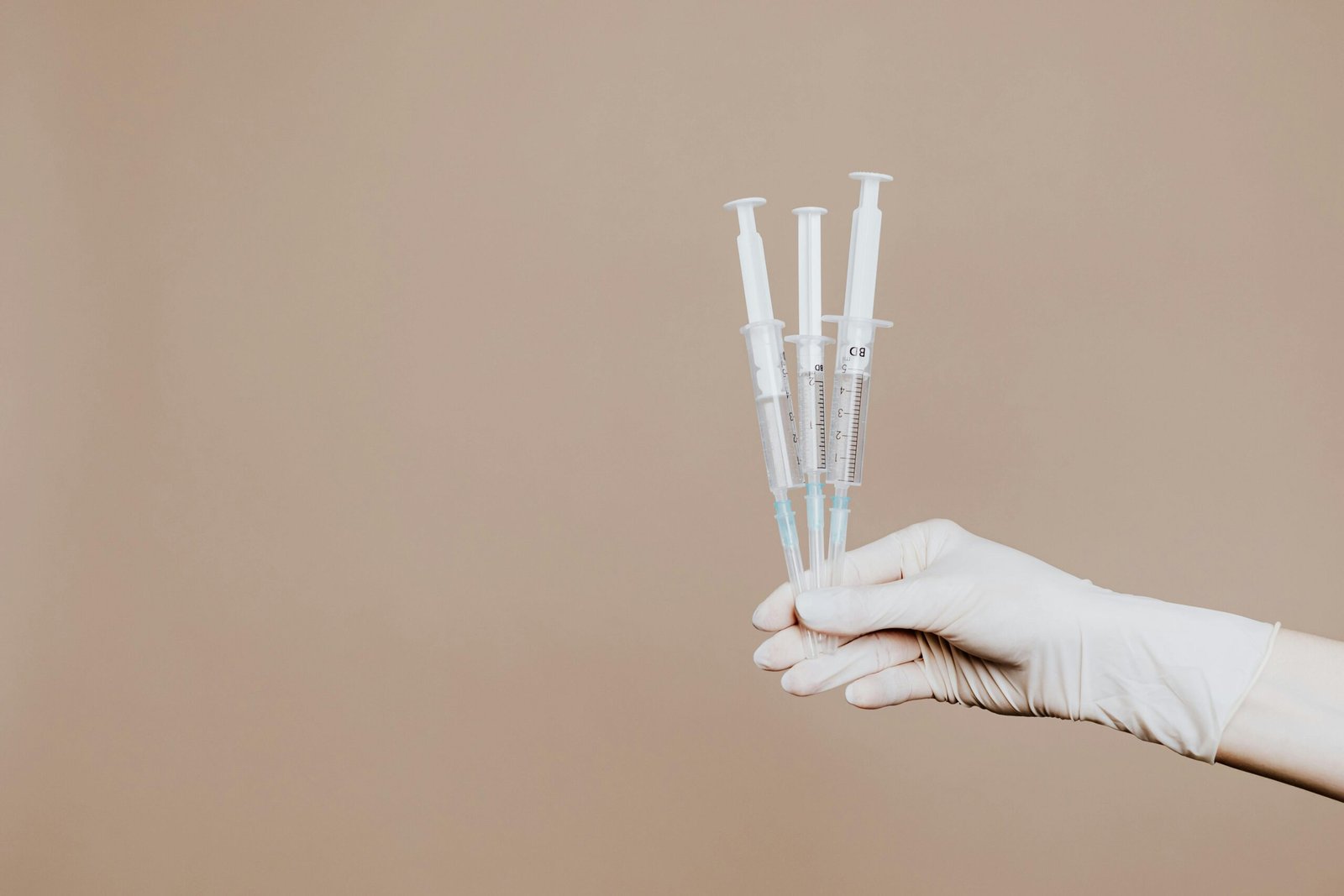 A gloved hand holds three sterile syringes, symbolizing healthcare and vaccination.